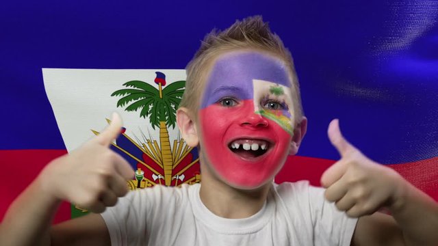 Joyful fan on the background of the flag of Haiti. Happy boy with painted face in national colors. The young fan rejoices in the victory of his beloved team. Success. Victory. Triumph.
