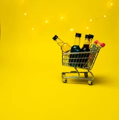  mini shopping cart full of small alcohol bottles yellow background © Roman