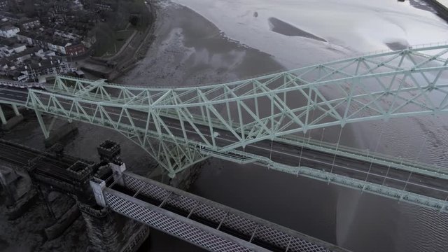 Aerial view arched green steel bridge & railway crossing over river reflections sunrise. Birds eye dolly rising right.