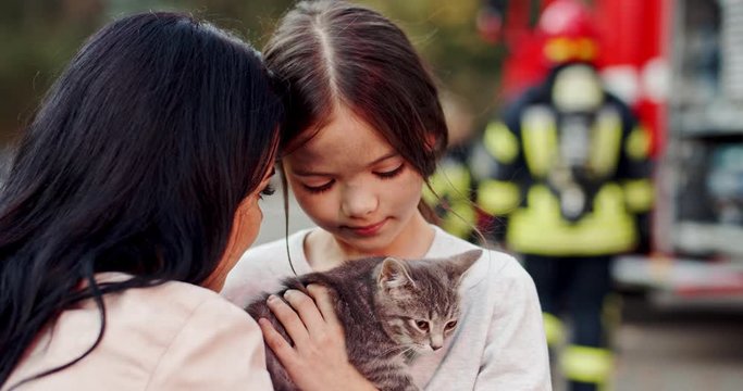 Close up of the Caucasian happy saved mother and small daughter hugging and holding kitty cat outside after fire.