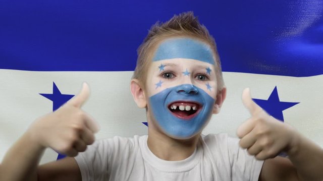 Joyful fan on the background of the flag of Honduras. Happy boy with painted face in national colors. The young fan rejoices in the victory of his beloved team. Success. Victory. Triumph.
