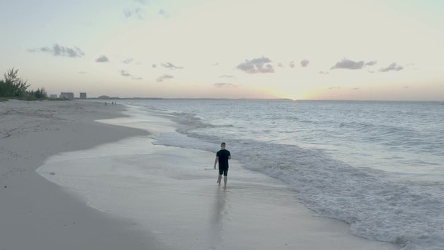 Aerial view of the beach with turquoise ocean on Turk and Caicos Caribbean Island, Providenciales. Man walking along beach at sunset. Drone footage, following