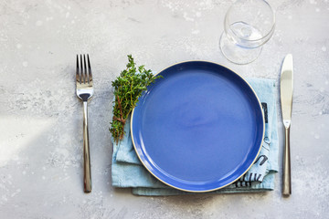 Blue ceramic plate, linen napkin, knife and fork. Dinner plate setting, top view. Mock up.