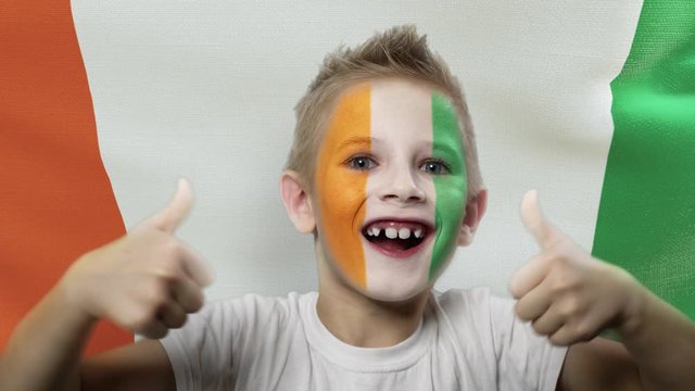 Joyful fan on the background of the flag of Ivory Coast. Happy boy with painted face in national colors. The young fan rejoices in the victory of his beloved team. Success. Victory. Triumph.