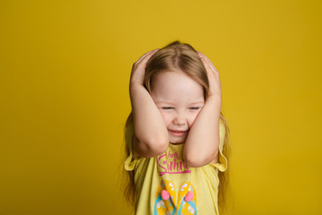 Portrait of scared little girl closing head by hands posing isolated at yellow studio background...