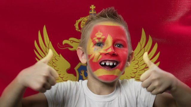 Joyful fan on the background of the flag of Montenegro.. Happy boy with painted face in national colors. The young fan rejoices in the victory of his beloved team. Success. Victory. Triumph.