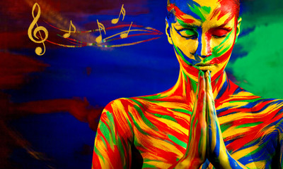 Color art face and body painting for inspiration. Woman in namaste yoga asana listen music. Closeup portrait of the bright beautiful girl with colorful make-up and bodyart and music notes.