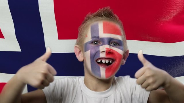 Joyful fan on the background of the flag of Norway. Happy boy with painted face in national colors. The young fan rejoices in the victory of his beloved team. Success. Victory. Triumph.