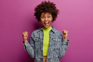 Achievement, celebration and win concept. Overemotive triumphing woman with Afro hairstyle, smiles...