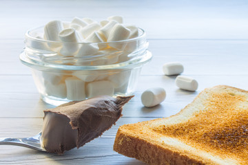 Food photo. Toasted toast, a spoonful of chocolate paste and white marshmallows in a glass jar with...