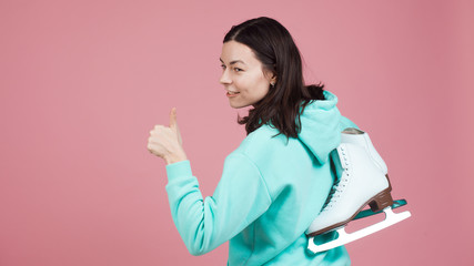 Figure skating, Hobbies and a healthy active lifestyle. A cheerful girl in a bright hoodie with skates on her shoulder
