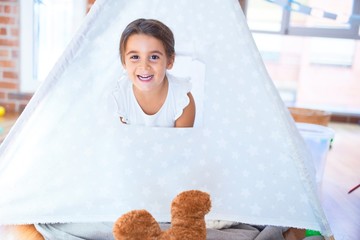Adorable toddler sitting on the floor inside tipi around lots of toys at kindergarten © Krakenimages.com