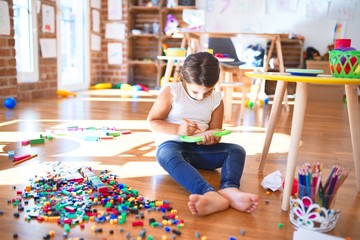 Adorable toddler drawing using digital board around lots of toys at kindergarten