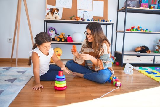 Beautiful teacher and toddler building pyramid using hoops around lots of toys at kindergarten