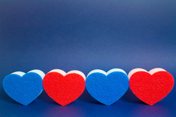 Obraz premium Four red and blue heart shape dishwasher sponge in the foreground on the blue background