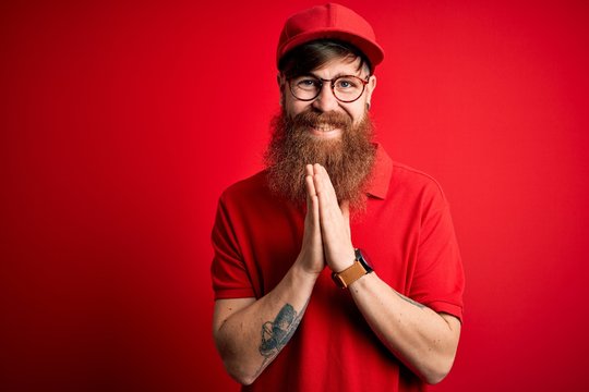 Young handsome delivery man wearing glasses and red cap over isolated background praying with hands together asking for forgiveness smiling confident.