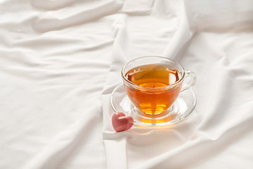 Morning tea with heart shaped candy on white bed sheet, copy space