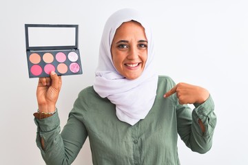 Young Arab woman wearing hijab showing makeup blush palette over isolated background with surprise face pointing finger to himself