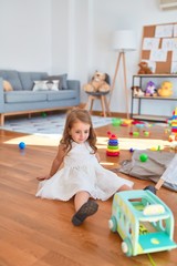 Adorable blonde toddler playing with car toy around lots of toys at kindergarten