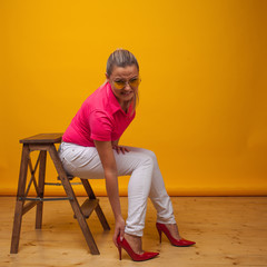 young woman suffers from uncomfortable high-heeled shoes, portrait in the Studio on a yellow...