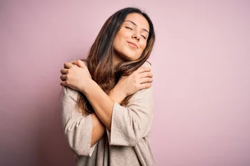 Poster Young beautiful brunette woman wearing casual sweater standing over pink background Hugging oneself happy and positive, smiling confident. Self love and self care © Krakenimages.com