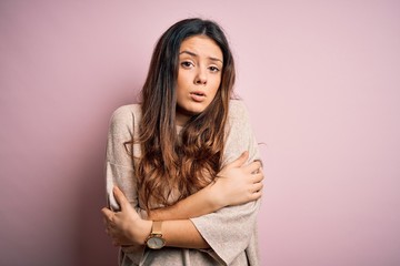 Young beautiful brunette woman wearing casual sweater standing over pink background shaking and...