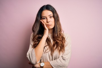 Young beautiful brunette woman wearing casual sweater standing over pink background thinking...