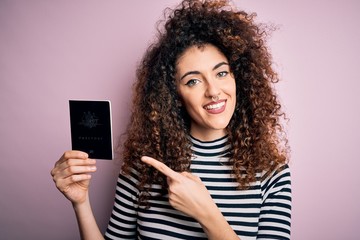 Beautiful tourist woman with curly hair and piercing holding australia australian passport id very happy pointing with hand and finger