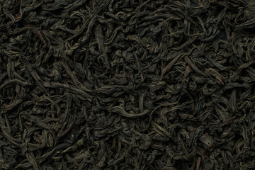 Black large-leaf tea as a background. Texture of dry black tea leaves. Black background