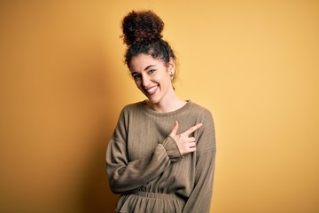 Fototapeta na wymiar Young beautiful brunette woman with curly hair and piercing wearing casual dress cheerful with a smile of face pointing with hand and finger up to the side with happy and natural expression on face