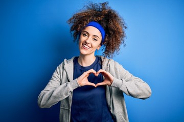 Young beautiful sportswoman with curly hair and piercing standing wearing sportswear smiling in love showing heart symbol and shape with hands. Romantic concept.