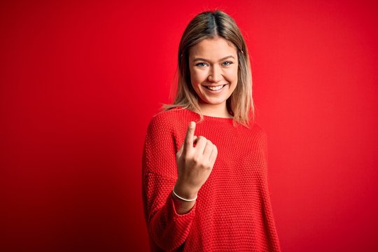 Young beautiful blonde woman wearing casual sweater over red isolated background Beckoning come here gesture with hand inviting welcoming happy and smiling