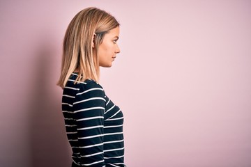 Young beautiful blonde woman wearing casual striped sweater over pink isolated background looking...