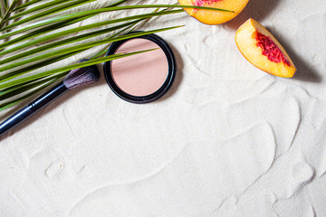 Dry cosmetic decorative product in round refile lies on the sand, surrounded by bright fruits,...