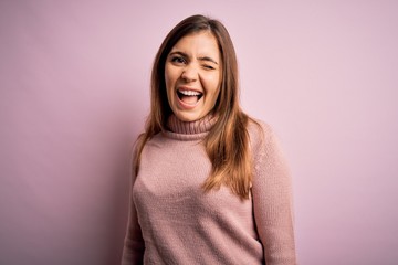 Fototapeta premium Beautiful young woman wearing turtleneck sweater over pink isolated background winking looking at the camera with sexy expression, cheerful and happy face.