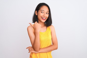Young chinese woman wearing yellow casual t-shirt standing over isolated white background smiling with happy face looking and pointing to the side with thumb up.