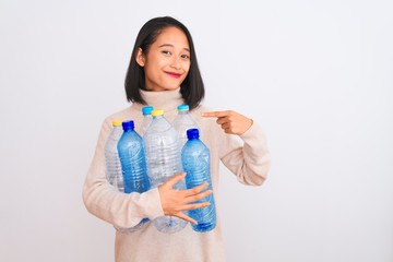 Young beautiful chinese woman recycling plastic bottles over isolated white background with surprise face pointing finger to himself