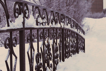 Black forged bridge with a beautiful ornament in the snow in the winter Park. Selective focus....