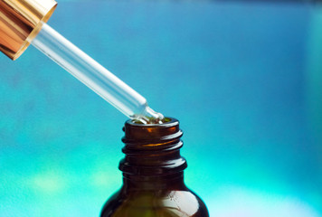 Cosmetic pipette with drops of cosmetic oil close-up on a colored background. Essential oil falling...