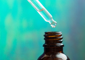 Cosmetic pipette with drops of cosmetic oil close-up on a colored background. Essential oil falling...