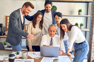 Group of business workers smiling happy and confident. One of them sitting and partners standing around. Working together with smile on face looking at the laptop at the office