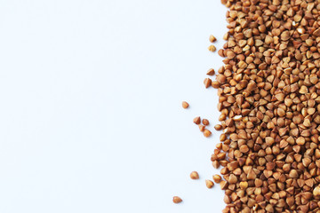 Raw buckwheat of a beautiful brown color is scattered on the right on a light background. Selective focus on grains. Copy space. Background with grits