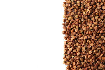 Raw buckwheat of a brown color is scattered on the right on a light background. Selective focus on grains. Copy space. Background with grits