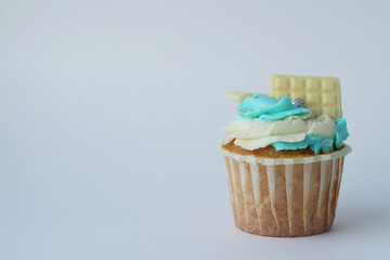 Beautiful fresh cupcake with blue and white cream, decorated with white chocolate bars and shiny silver balls on a light background. Selective focus. Homemade cake. Side view