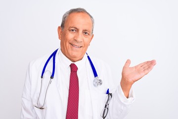 Senior grey-haired doctor man wearing stethoscope standing over isolated white background smiling cheerful presenting and pointing with palm of hand looking at the camera.