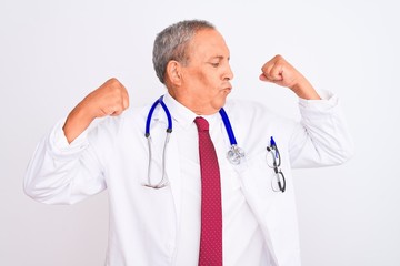Senior grey-haired doctor man wearing stethoscope standing over isolated white background showing arms muscles smiling proud. Fitness concept.