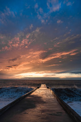 Fototapeta na wymiar Big waves breaking on a stone pier in stormy weather with a bright sunset, a big tide. Black Sea. Sochi, February.