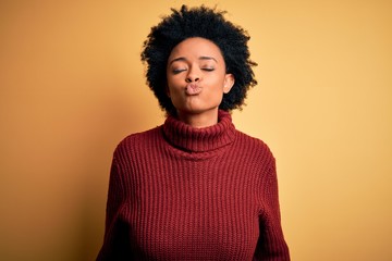 Fototapeta na wymiar Young beautiful African American afro woman with curly hair wearing casual turtleneck sweater looking at the camera blowing a kiss on air being lovely and sexy. Love expression.