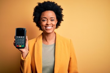 Young African American afro woman with curly hair holding dataphone payment device with a happy...