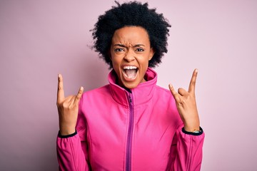 Fototapeta na wymiar Young African American afro sportswoman with curly hair wearing sportswear doin sport shouting with crazy expression doing rock symbol with hands up. Music star. Heavy concept.